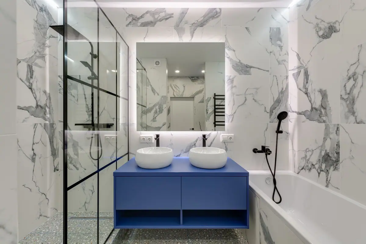 Bañera con mampara de vidrio templado y perfil negro en un baño de mármol