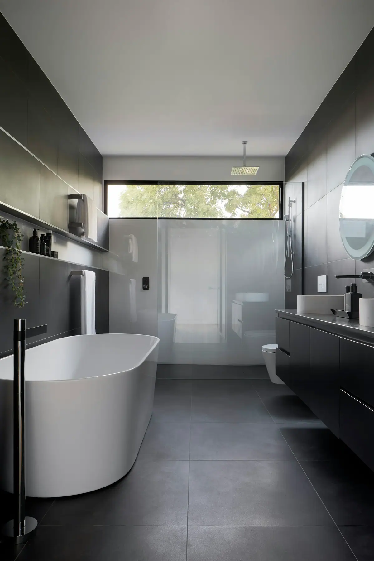 Baño en tonos oscuros con griferías negras, bañera exenta y ducha de vidrio