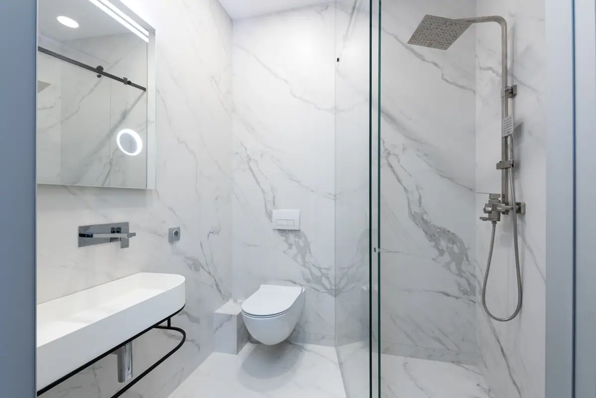 Baño de mármol blanco con box de ducha de vidrio templado de alta seguridad y ducha de lluvia